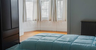 bedroom inside drayton house with bed with blue bedspread and 3 windows