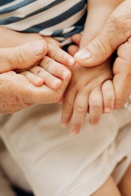 Close-up of an older person’s hands gently holding the small hands of a young child